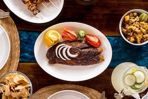 A plate of grilled fish with lemon slices, tomatoes, and onions, accompanied by a bowl of salad and a plate of skewers.