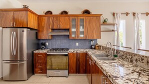 Eine Küche mit Holzausstattung, einem Edelstahl-Kühlschrank, einem Gasherd und einer Marmorarbeitsplatte.