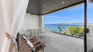 Un balcón con vista al mar, sillas blancas y una mesa.