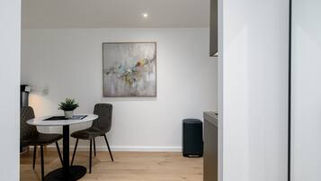 A modern dining area with a round table, two chairs, a potted plant, and a large abstract painting on the wall.
