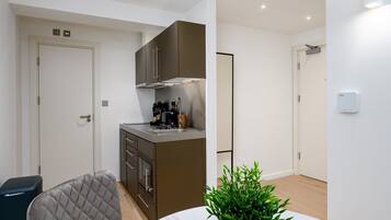 A compact kitchen with a built-in stove, a coffee machine, and a small countertop. There is a chair and a table with a potted plant.