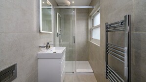 Un baño moderno con ducha de vidrio, lavamanos blanco y toallero empotrado.