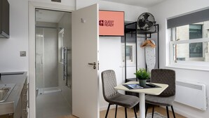 Habitación de hotel moderna con ducha, una mesa con sillas, un cartel que indica 'GUEST READY' y una ventana con vistas al exterior.
