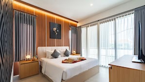 A modern hotel room with a large bed, wooden paneling, a desk, and a view of the city.
