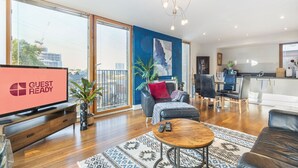 Ein modernes Wohnzimmer mit großem Fernseher, einer Couch, einem Couchtisch und einem Essbereich mit Stühlen und Tisch.