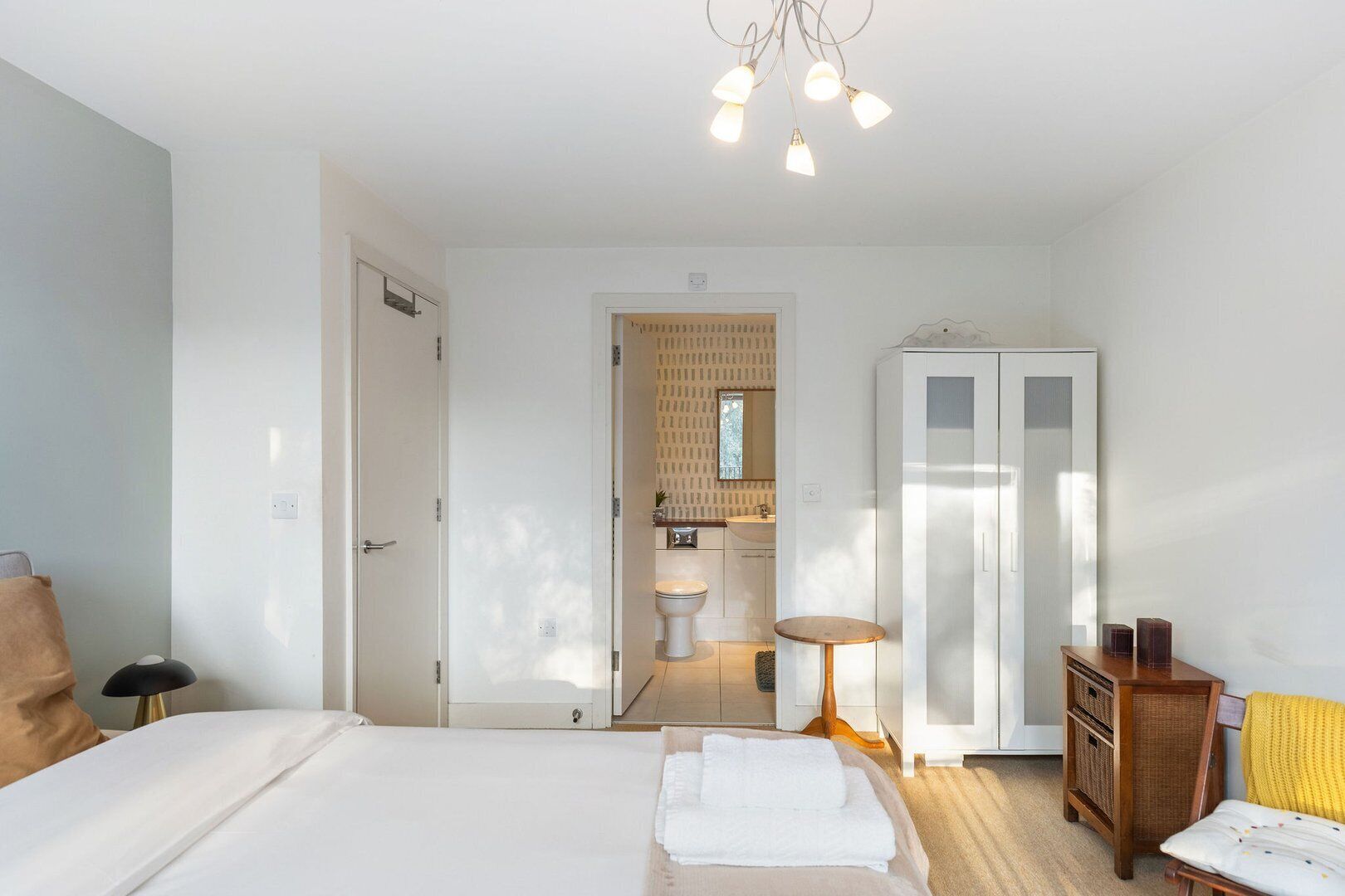 A bedroom with a bed, bedside table, wardrobe, and a bathroom visible through an open door.