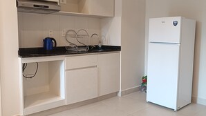Una cocina con armarios blancos, una encimera negra, un refrigerador blanco y una tetera azul.