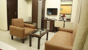 Een hotelkamer met een bank, fauteuil en een salontafel. Er is een televisie aan de muur bevestigd en een tafeltje met een waterfles.