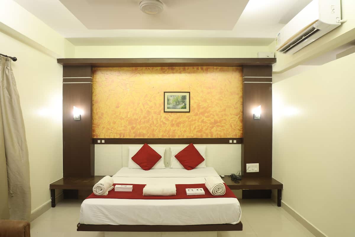 A hotel room with a bed, a red and white headboard, a painting on the wall, and an air conditioning unit.