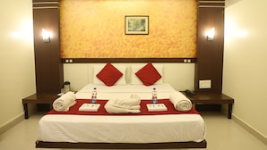 Hotelkamer met een groot bed, rode kussens, een hoofdbord met een afbeelding en twee nachtkastjes met waterflessen en handdoeken.