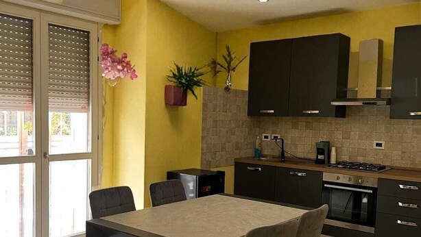 A modern kitchen with a dining area, featuring a large table and chairs, a built-in oven, and a stove. - Poetto di Cagliari vacation home 2 steps from the sea, relax sport and fun (Cagliari)