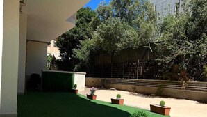 An outdoor area with artificial green turf, potted plants, and a building in the background. - Poetto di Cagliari vacation home 2 steps from the sea, relax sport and fun (Cagliari)