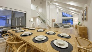 Un vaste espace dédié à la salle à manger, avec une longue table en bois dressée pour le repas, un escalier et un salon offrant une vue agréable.