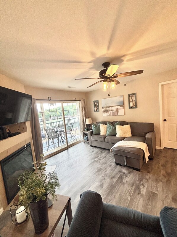 A spacious living room with a grey sofa, a coffee table with a plant, and a ceiling fan.