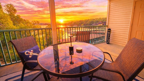Un balcón con mesa y sillas de vidrio, con vistas a un atardecer.