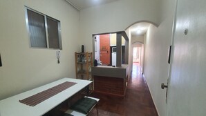 Un pasillo estrecho que desemboca en una zona de cocina, con un refrigerador, pileta y una estantería de madera con utensilios de cocina.
