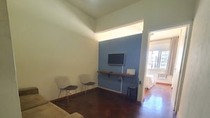 Una habitación con piso de madera, un televisor montado en la pared, dos sillas de estructura metálica y una mesita.