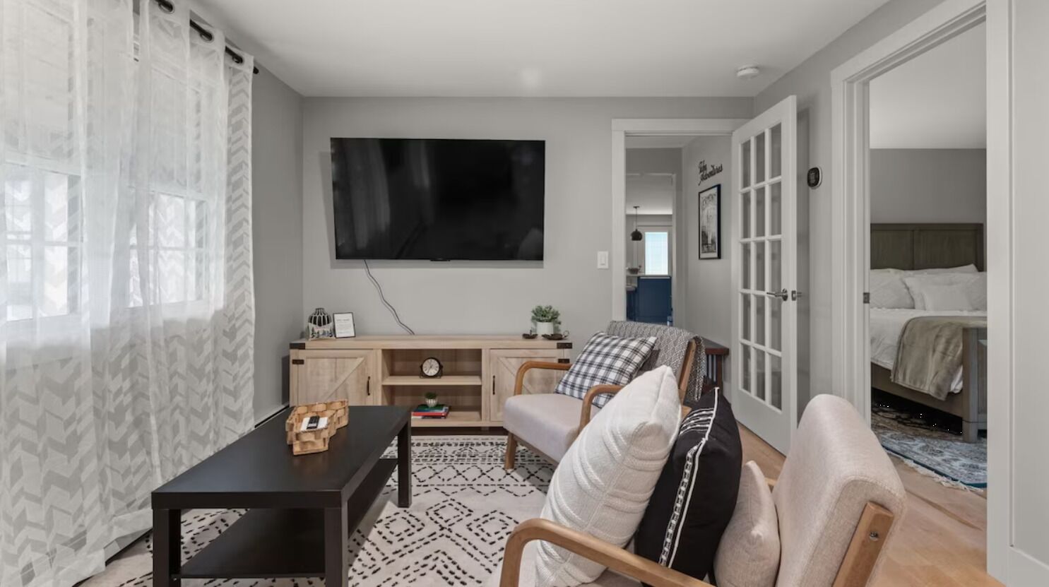 Un salon moderne avec un téléviseur à écran plat fixé au mur, une table basse en bois, un canapé agrémenté de coussins à motifs et un tapis à motifs.