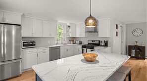 A modern kitchen with white cabinetry, stainless steel appliances, and a marble island.