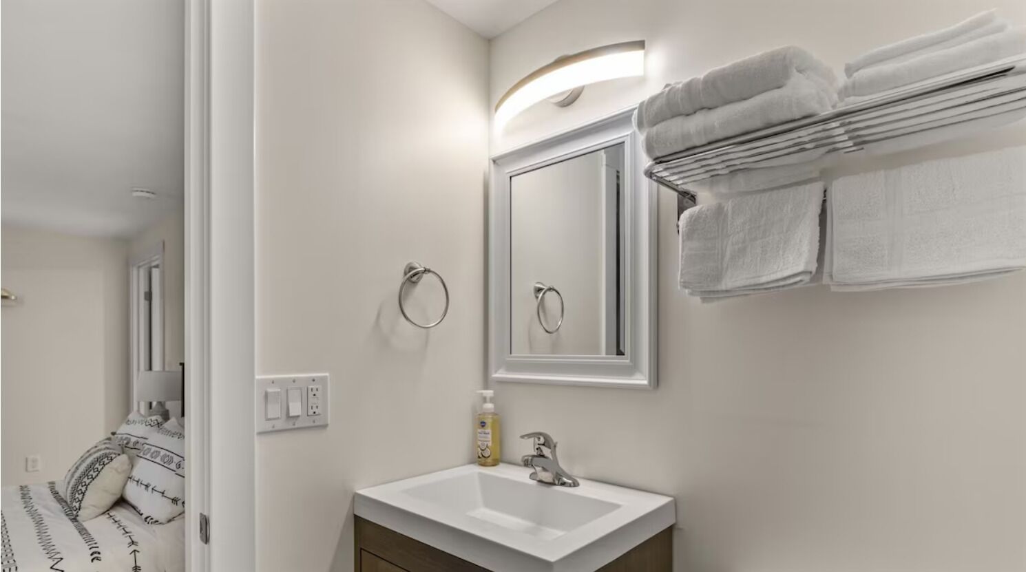 A modern bathroom with a white sink, a mirror, and a towel rack with folded towels.