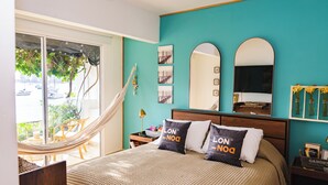 Un dormitorio con una hamaca, una cama con dos almohadas, una mesita de noche, un espejo y obras de arte en la pared.