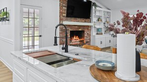 A modern kitchen with a marble countertop, a built-in brick fireplace, and a flat-screen TV above it. - Stay Local Fantastic 4 Bedroom Near the Rez Sleeps 16 (Brandon)