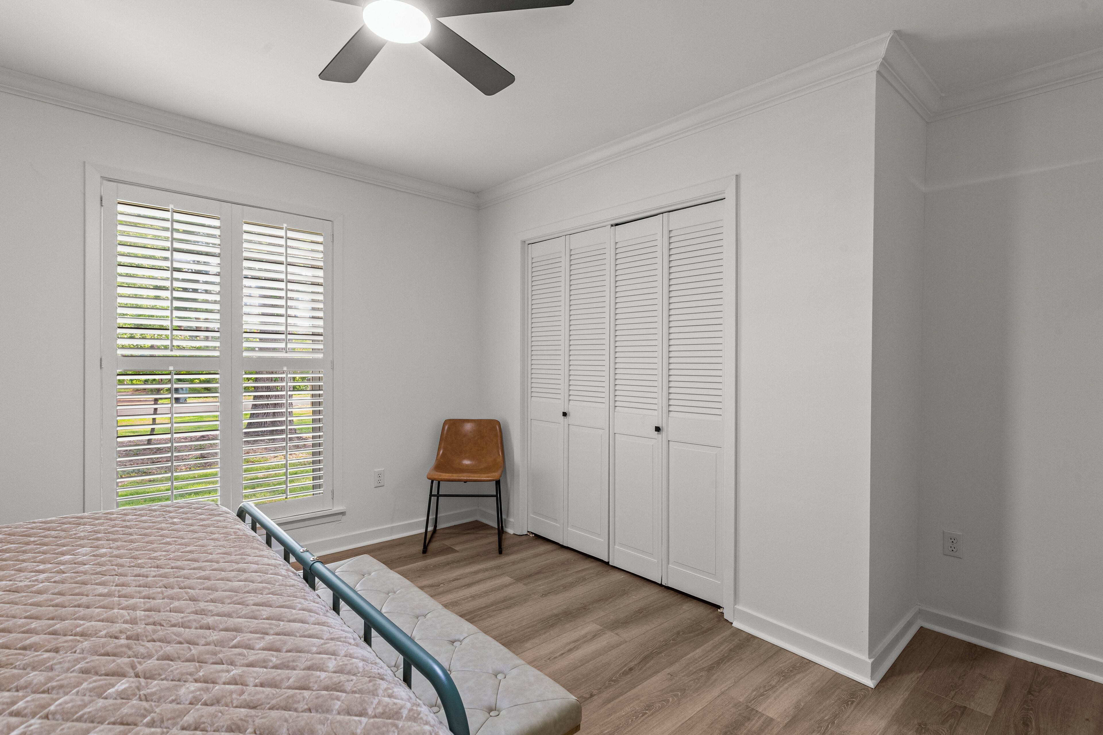 A bedroom with a bed, a chair, a ceiling fan, and a set of white closets.