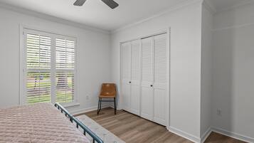 A bedroom with a bed, a chair, a ceiling fan, and a set of white closets.