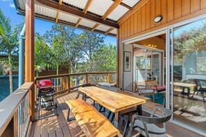 An outdoor deck with a wooden table and chairs, a barbecue grill, and a glass door leading to an interior space.