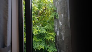 A view through a window with a brick wall and dense foliage outside. - Cozy 3BR Near Beach, Tranquil Fish Pond & Parking (Đà Nẵng)