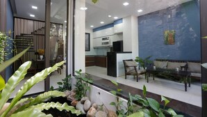 A modern kitchen with white cabinets and a black countertop, a dining area with a table and chairs, and a living area with a sofa and coffee table. - Cozy 3BR Near Beach, Tranquil Fish Pond & Parking (Đà Nẵng)