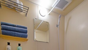 A bathroom with a toilet, a bathtub, and a shower. There are towels and toiletries on a shelf above the toilet.