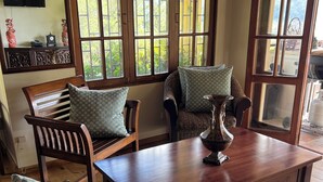 A room with a wooden table, two chairs, and a sofa with patterned cushions. There are large windows with multiple panes, and a television mounted on the wall. - Summit LuxeVilla (Constanza)