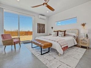 Une chambre à coucher moderne avec un grand lit, un ventilateur de plafond, une fenêtre donnant sur le désert et une petite table de chevet avec une lampe.