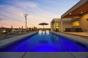 Une piscine à l’eau bleutée, entourée de chaises longues et d’une terrasse en bois.