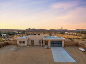 Une maison de plain-pied avec un garage, entourée d’une cour clôturée, et un paysage désertique en arrière-plan.