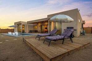 A modern outdoor pool area with lounge chairs and a wooden deck. - Desert Spa: Heated Pool · Hot Tub · Sauna · Cold Plunge · New Home - Joshua Tree (Joshua Tree)