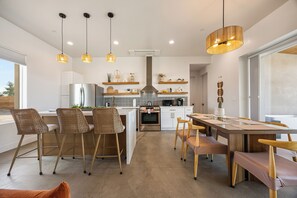 Une cuisine moderne dotée d’un îlot central, de luminaires suspendus et d’un coin repas avec une table et des chaises en bois.