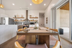 Une cuisine moderne dotée d’un îlot central, d’appareils électroménagers intégrés et d’un coin repas avec une table en verre et des chaises en bois.