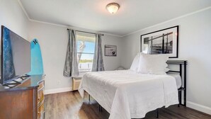 Un dormitorio con cama, cómoda, luz de techo, ventana con cortinas e imagen enmarcada en la pared.