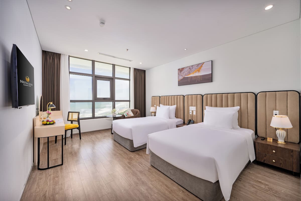 Een hotelkamer met twee bedden, een bureau met stoel, een televisie en een groot raam met gordijnen.