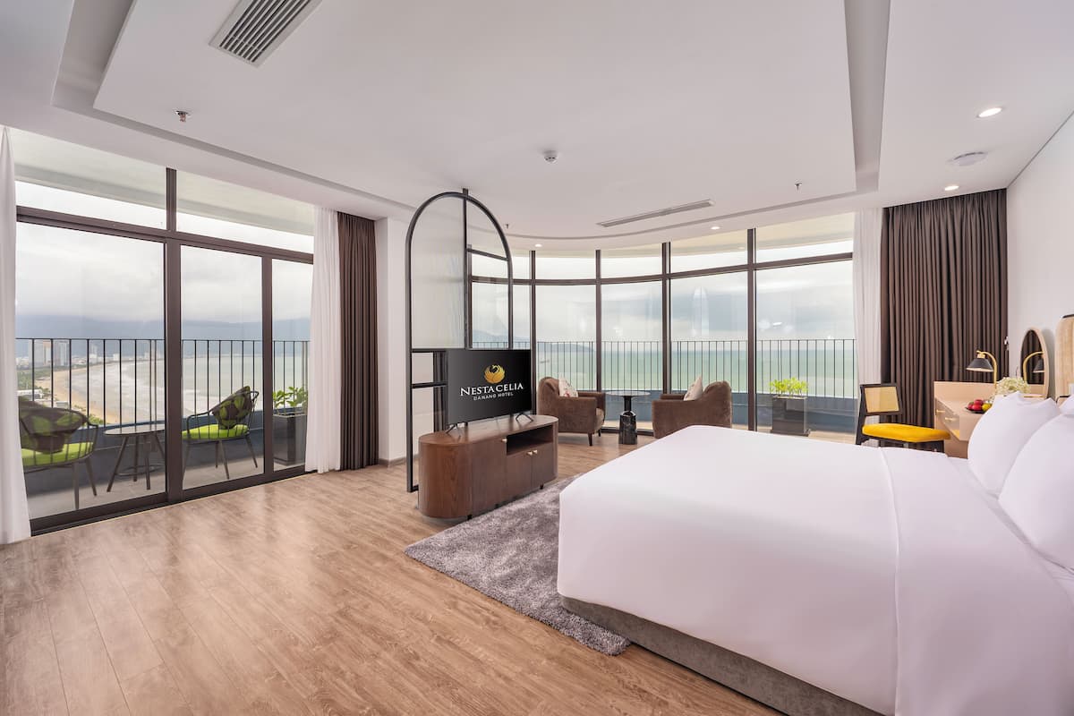 Een moderne hotelkamer met een groot bed, een televisie, een balkon met stoelen en uitzicht op de stad.