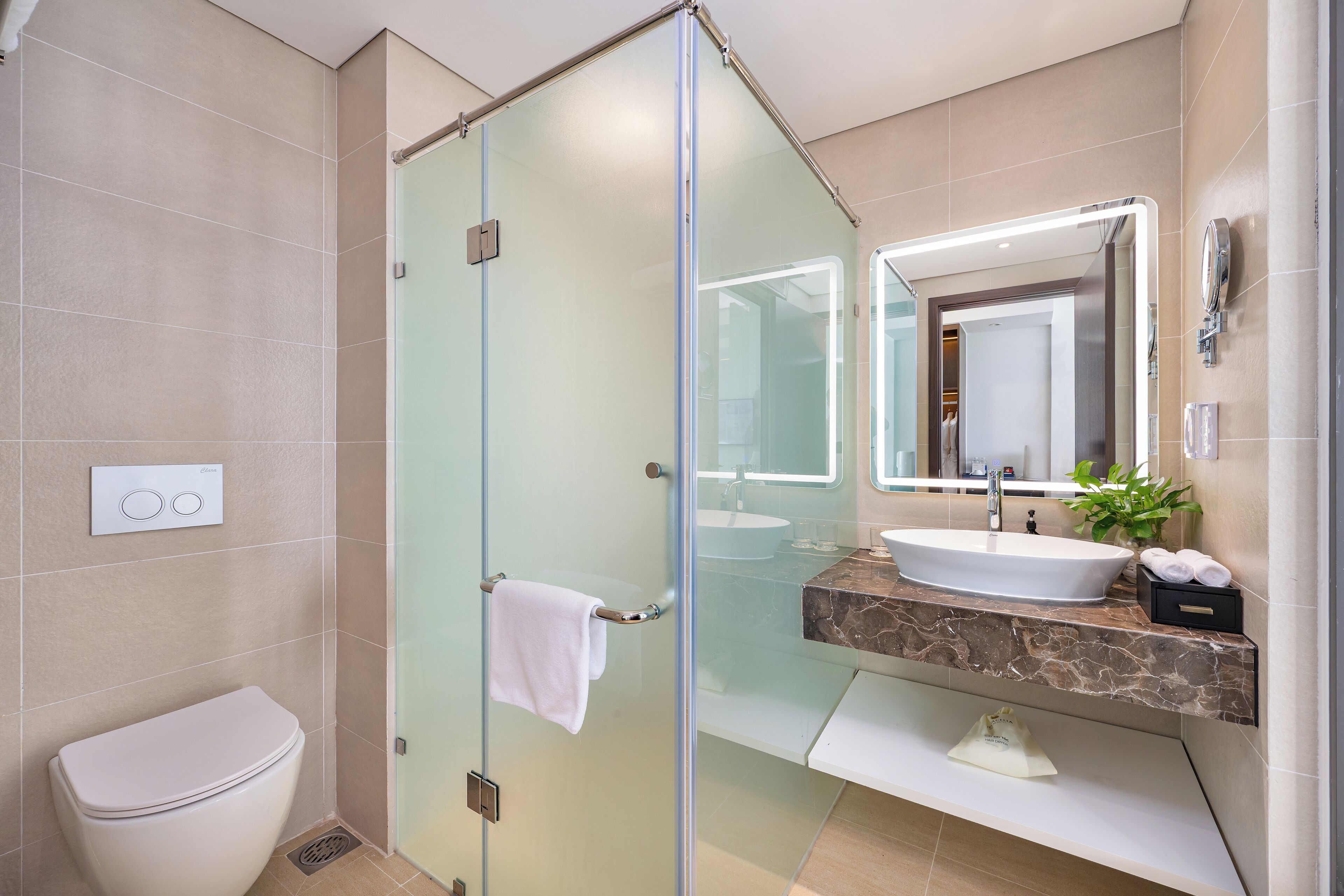 A modern bathroom with a glass shower enclosure, a white toilet, a marble sink, and a large mirror.