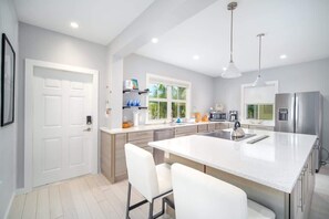 A modern kitchen with a large island, white cabinetry, stainless steel appliances, and pendant lighting.