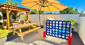 A wooden pergola with a picnic table and an umbrella, a blue and white play structure, and a white wall with a fence. - Coastal Chic 2BR/1b / Long Beach (Long Beach)