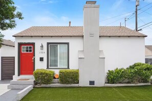 A modern single-story house with a red door, numbered 1504, a chimney, and a well-maintained lawn. - Coastal Chic 2BR/1b / Long Beach (Long Beach)