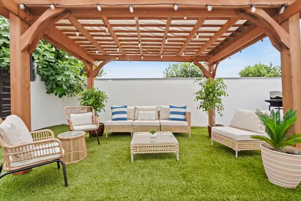 A covered patio area with wicker furniture, a white sofa set, and a small table. - Coastal Chic 2BR/1b / Long Beach (Long Beach)