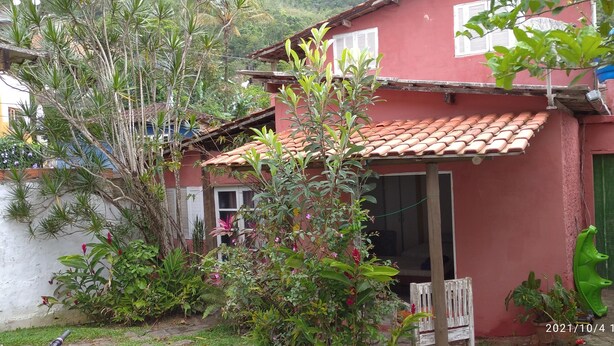A red house with a tiled roof, surrounded by lush greenery and a small garden.