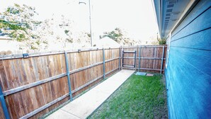 A backyard with a wooden fence, a concrete pathway, and a grassy area. - Cozy Studio Min to JPS, Medical City, Historic District, Zoo, Water Gardens (Fort Worth)