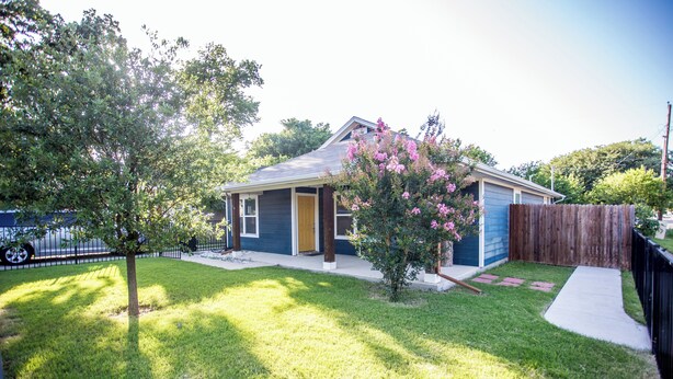 A residential house with a front yard, a wooden fence, and a tree with pink flowers. - Cozy Studio Min to JPS, Medical City, Historic District, Zoo, Water Gardens (Fort Worth)